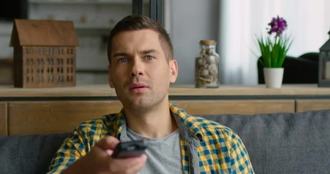 Young man is sitting on a sofa, switching TV on Stock Footage 113616652
