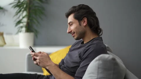 Young man sitting on the sofa texting on mobile phone Stock Footage 149244648