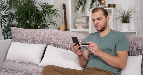 Young Man Sitting on Sofa Using Mobile Phone to Shopping Online with Credit Card Stock Footage 87912123