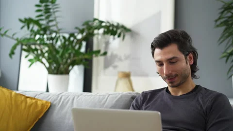 Young man sitting on the sofa using laptop Stock Footage 149244716