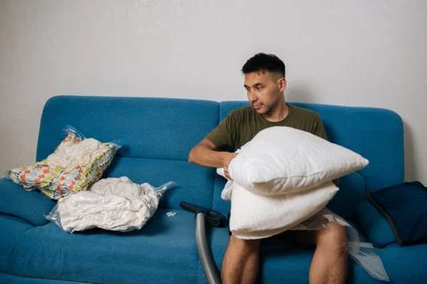Young man sitting on sofa, using vacuum storage bag to organize and compress Stock Photos