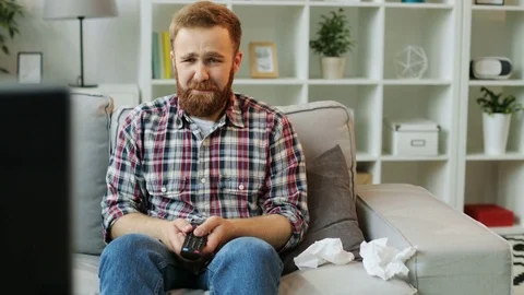 Young man sitting on a sofa, watching drama on the TV at home in the living room Stock Footage 76236903