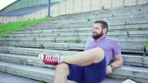 Young man sitting on stairs reading newspaper and ralxing, slider shot. 库存影片 67607741