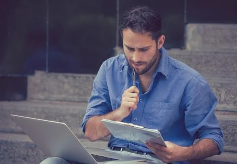 Young man sitting on steps outside corporate city building using a laptop Stock Photos