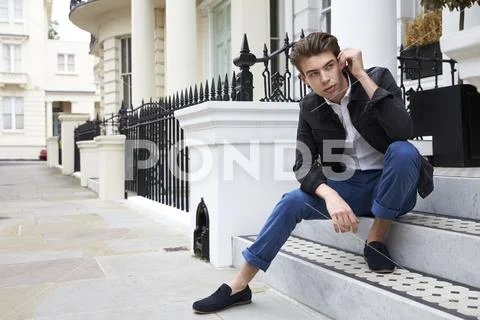 Young man sitting on steps outside house looking down street Stock-Fotos