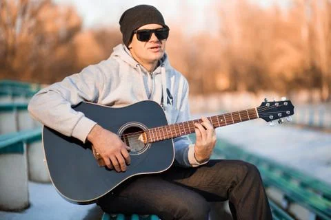Young man sitting on steps playing guitar and singing, music concept Stock Photos