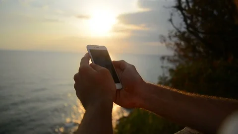 Young man is sitting on a stone and using smartphone near the sea. Portrait of Stock Footage 79410550