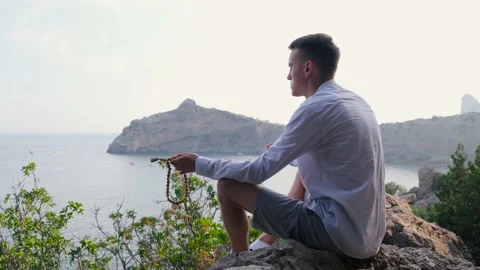 Young man sitting on a stone cliff overlooking the sea and meditating Stock Footage 166576597