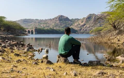 Young Man Sitting on Stone by Pristine Lake at Morning Stock Photos