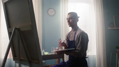 Young Man Is Sitting On Stool and Painting on Canvas 스톡 동영상 136596725