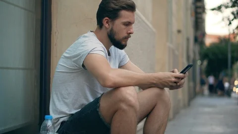 Young man sitting on the street using smartphone Stock Footage 118944284