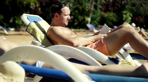 Young man sitting on sunbed and reading book by the pool   Stock Footage 1068696
