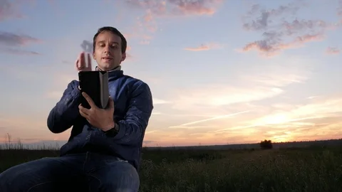 A young man is sitting at sunset and talking on a video call on a tablet Stock Footage 76922379