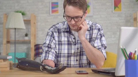 Young man sitting at a table adjusts a prosthetic arm through a smartphone Stock Footage 119384426