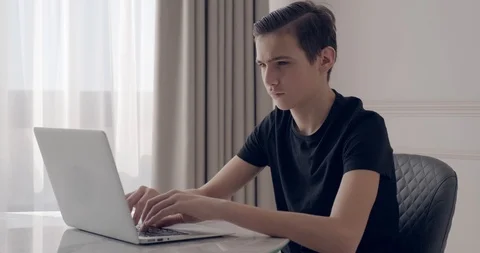 Young man sitting on the table and using laptop. Teen boy sitting on desk at  Stock Footage 106088180