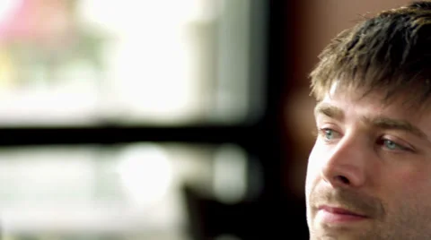 A young man sitting at a table in a cafe looks into the camera and smiles Stock Footage 33993473