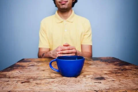 Young man sitting at table with cup of coffee Photos