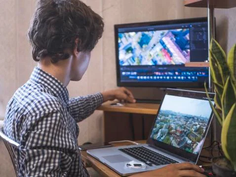 Young man sitting at the table editing video using laptop and external monito Stock Photos