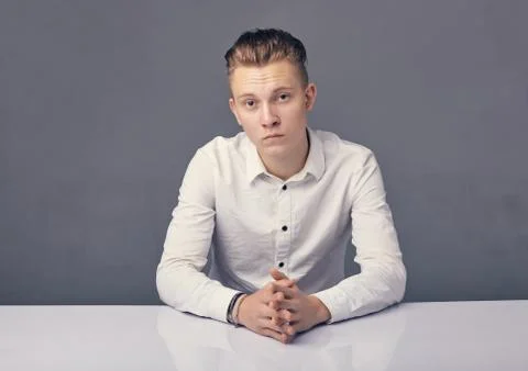 Young man sitting at a table on a gray background. Stock Photos