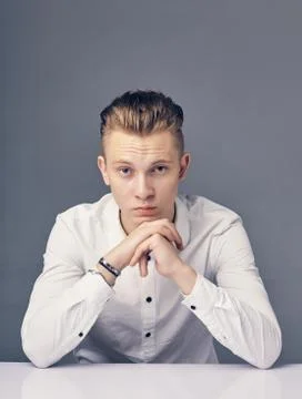 Young man sitting at a table on a gray background. Stock Photos