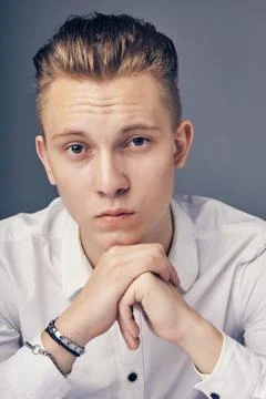 Young man sitting at a table on a gray background. Stock Photos