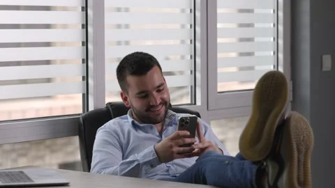 Young man is sitting at table having his legs on desk, relaxing Stock Footage 194118913