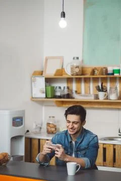 Young man sitting at a table in the kitchen with his mobile phone Stock Photos
