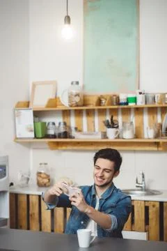Young man sitting at a table in the kitchen with his mobile phone Stock Photos