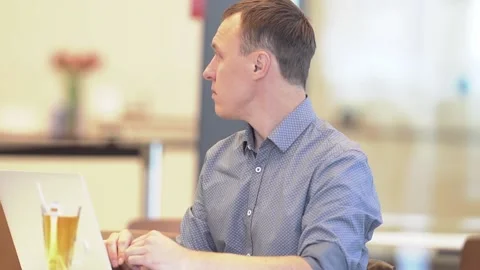 A young man sitting at a table with a laptop in a cafe looks away. A slow-motion Stock Footage 201210587