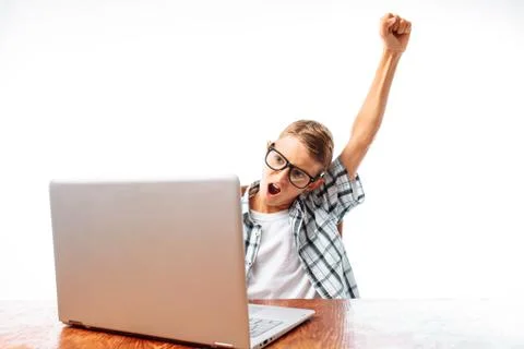A young man sitting at a table with a laptop, happy victory raising his hand  Stock Photos