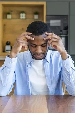 Young man sitting at a table in a modern kitchen, looking thoughtful and st.. Stock Photos
