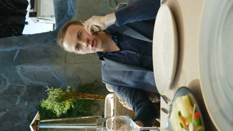 A young man is sitting at a table in a restaurant and talking on the phone. Stock Footage 136813679