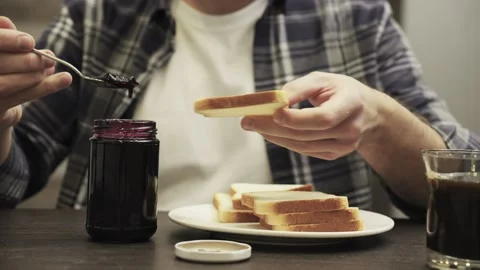 Young man sitting at table, spreading some jam on a toast. Slow motion Video stock 274384911
