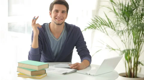 Young man sitting at table studying with books and laptop Video stock 28790566