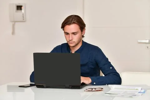Young man sitting on a table using a laptop next to some bills Stock Photos