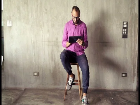 Young man sitting with tablet computer in front of concrete wall Stock Footage 77066361