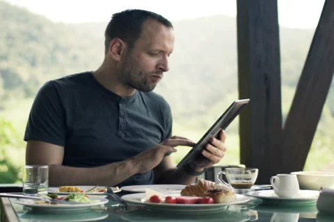 Young man sitting with tablet during breakfast on the terrace NTSC Stock Footage 51770460