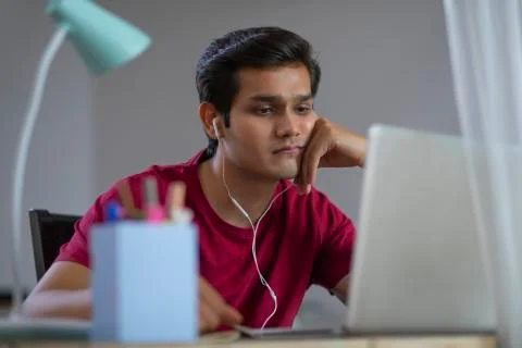 A YOUNG MAN SITTING TIRED WHILE ATTENDING ONLINE CLASS	 Stock Photos