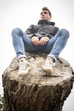 Young Man SItting On Top Of A Fallen Tree Up High Stock Photos