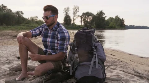 Young Man Sitting in the Wild and Putting Headphones On Stock Footage 76467596