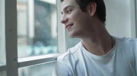 Young man sitting by the window and smiling waving to his friend Stock Footage 49775465