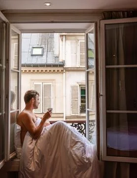 Young man sitting in a window looking out over the city Paris. Men enjoy sun in Stock Photos