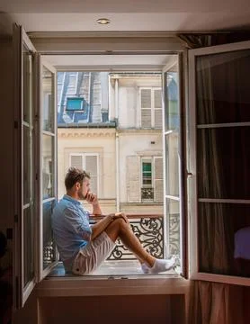 Young man sitting in a window looking out over the city Paris. Men enjoy sun in Stockfoto's