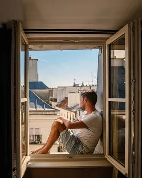 Young man sitting in a window looking out over the city Paris. Men enjoy s... Stock-Fotos