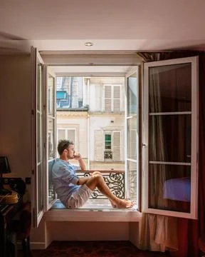 Young man sitting in a window looking out over the city Paris. Men enjoy s... Stock-Fotos