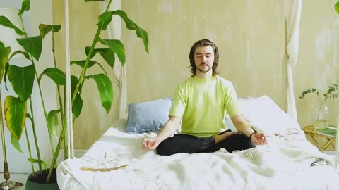 Young man sitting in yoga pose in bed and concentrating Stock Footage 141454945