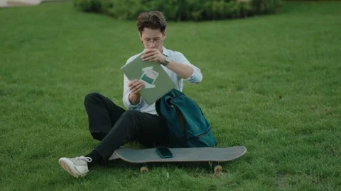Young Man with Skateboard and Backpack Working on Laptop in Park Stock Footage 309115491