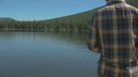 Young man skipping some rocks on a lake Stock Footage 77995938