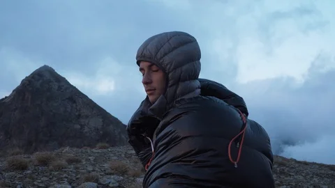 Young man in sleeping bag looking at mountain panorama, 4K Stock Footage 129611155