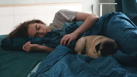 Young man sleeping in bed with his dog, the dog looks into the frame. 動画素材 196812730